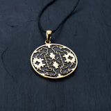 The Shipibo pendant from Kaya Movement, crafted from yellow brass, showcases intricate, maze-like designs and oxidized details. This striking gold pendant hangs elegantly from a black cord against a dark, textured background, featuring symmetrical patterns and geometric shapes that create an eye-catching visual effect.