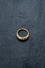 A ring from Kaya Movement's collection, the "Biomechanical - 18k Gold Septum 10mm - Alien Xenomorph," lies on a dark, textured surface. Featuring a braided or interwoven pattern around its band, this distinctive and elegant piece resembles cybernetic bio-organic jewelry.