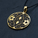 The Kaya Movement Shipibo pendant, known as Trippy jewelry, is a yellow brass shamanic pendant featuring intricate geometric and floral cutout designs. Attached to a black cord necklace, this psychedelic pendant showcases symmetrical patterns and oxidized details that shine against a dark background, highlighting its detailed craftsmanship.