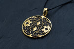 The Kaya Movement Shipibo pendant, known as Trippy jewelry, is a yellow brass shamanic pendant featuring intricate geometric and floral cutout designs. Attached to a black cord necklace, this psychedelic pendant showcases symmetrical patterns and oxidized details that shine against a dark background, highlighting its detailed craftsmanship.