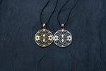 Two round Kaya Movement Shipibo Icaro pendants with intricate patterns featuring skull designs. One pendant is yellow brass with a black background and oxidized details, while the other is silver with a black background. Both are attached to black cords and set against a dark, textured surface.
