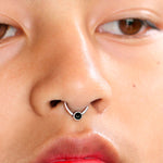 A close-up image of a person's face showcasing Kaya Movement's Black Onyx Silver Septum Jewelry - Seamless Nose Ring 8mm. The focus is on the nose and mouth area, highlighting the intricate details of the skin and lips, with the person's eyes partially visible at the top of the frame.