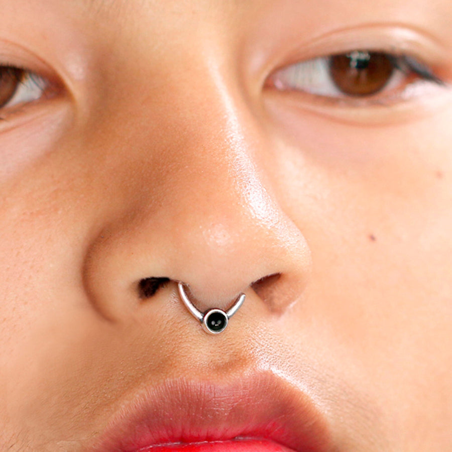 A close-up image of a person's face showcasing Kaya Movement's Black Onyx Silver Septum Jewelry - Seamless Nose Ring 8mm. The focus is on the nose and mouth area, highlighting the intricate details of the skin and lips, with the person's eyes partially visible at the top of the frame.