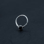A simple yet sophisticated septum ring, featuring a smooth, round black onyx gemstone set in its center. This elegant piece, part of Kaya Movement's exclusive Silver 925 Jewelry collection, is displayed against a dark, textured background, highlighting its minimalist design and polished finish.
