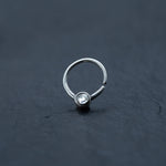 A close-up of the Zircon Silver septum ring from Kaya Movement, featuring a small, clear Crystal Zircon at the center. The 8mm, 18g seamless horseshoe piercing is set against a dark, textured background, showcasing its simple yet elegant design.