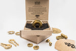 An opened cardboard box with "Kaya Movement" branding contains a gold statement ring displayed on black padding. Surrounding the box are additional gold jewelry pieces, including rings, bracelets, and pendants with snake motifs, spread on a white surface. A hint of the Minimalist Silver Finish 316L Stainless Steel Septum with Turquoise "Turia" glimmers amidst the collection.