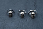 An image of three Kaya Movement Skull Ball Closure Rings, from the Punk Goth Hoop earrings collection, artistically arranged in a row on a dark, textured surface. The rings are made of Stainless Steel 316L and feature intricately detailed skull charms with visible eye sockets, nasal cavities, and teeth.