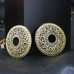 From Kaya Movement, a pair of Gold breast buttons piercing jewelry rings with an intricate design features a circular hole in the center. These non-piercing teat tassels showcase ornate patterns of swirls and dots, reminiscent of antique gold filigree. Perfect as fake teat piercings or body jewelry shields, they are set against a dark background.