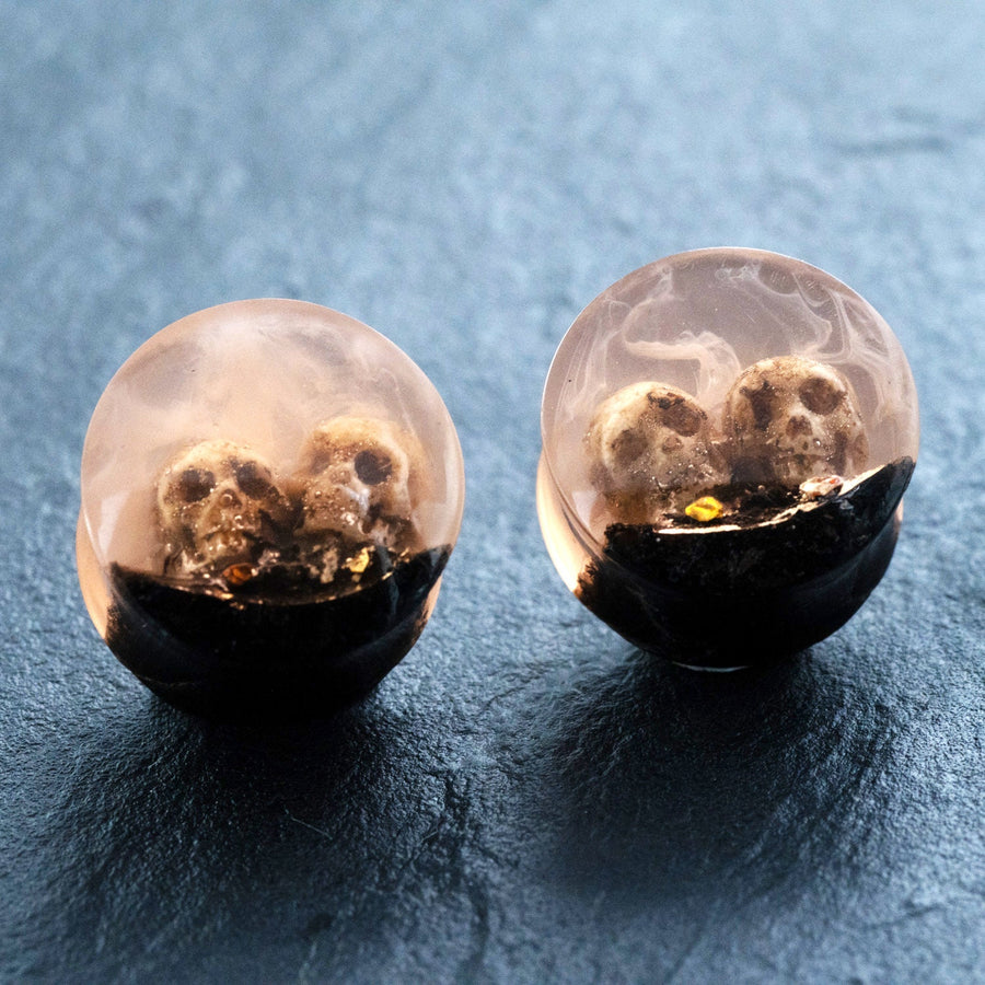 Introducing the Handmade Epoxy Double Flare Flesh Tunnels with Skull and Gothic Design by Kaya Movement. These earrings, available in 12mm-16mm sizes, feature embedded tiny skulls encased in a combination of transparent and black resin, creating a striking miniature diorama effect. The gothic jewelry showcases skulls partially surrounded by the black resin, giving them an eerie rise-from-the-darkness appearance.