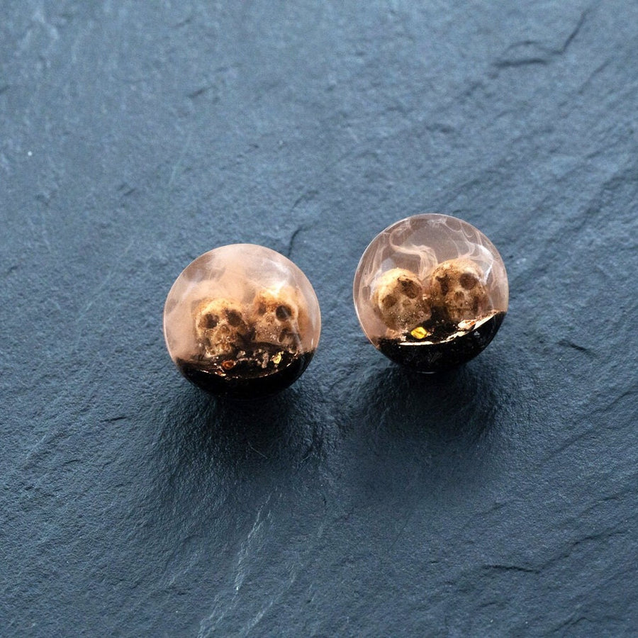 Introducing Kaya Movement's Handmade Epoxy Double Flare Flesh Tunnels with Skull and Gothic Design, available in 12mm-16mm sizes. These stunning gauged ear stretching pieces feature detailed skulls encased in a semitransparent epoxy material. Against a dark, textured background, the intricate artistry of this gothic jewelry is beautifully highlighted.