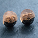 Introducing the Kaya Movement Handmade Epoxy Double Flare Flesh Tunnels with Skull and Gothic Design, available in 12mm-16mm gauges. These striking pieces of gothic jewelry feature clear resin earrings with small skulls embedded inside a gradient effect that transitions from transparent to a darker base. The skulls are partly embedded in a black layer at the bottom, making these earrings an eye-catching addition to any collection.