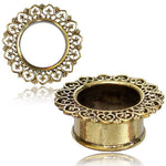 Two Indian Gold Brass Ear Gauges with intricate openwork designs from Kaya Movement are shown. One is standing on its edge, displaying its ornamental rim, while the other lies flat, revealing its hollow center. Resembling mandala brass tunnels with a vintage gold appearance, these handmade ethnic ear plugs make a unique addition to any collection.