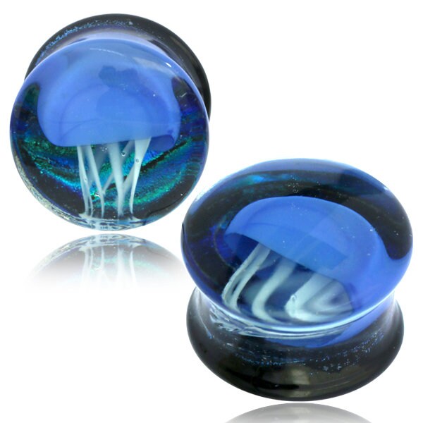 The Blue Glass Jellyfish Ear Plugs by Kaya Movement are handmade double flare flesh tunnels, featuring a mesmerizing blue jellyfish design inside. These unique ocean-themed pieces of body jewelry, available in 12mm-16mm sizes, showcase the translucent body and tentacles of the jellyfish that appear to be floating, creating a stunning three-dimensional effect.