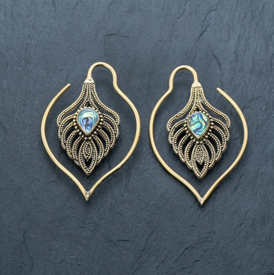 A pair of ornate, unisex handmade brass leaf ear weights by Kaya Movement, featuring intricate abalone shell inlays at the center. These Boho Hippie Tribal Earrings are perfect for those with gauged ears seeking unique jewelry and are displayed on a dark slate background.