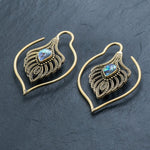 Unisex Handmade Brass Leaf Ear Weights with Abalone Shell from Kaya Movement, showcased against a dark slate background. These boho hippie tribal earrings, crafted in an open hoop style, feature intricate metalwork that resembles delicate leaves and gleaming abalone shells at the center, making them perfect for gauged ear jewelry enthusiasts who appreciate edgy urban fashion.