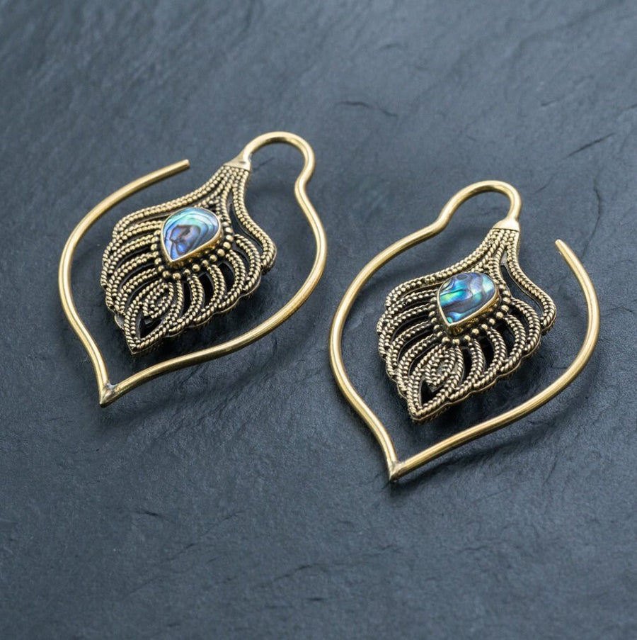 Unisex Handmade Brass Leaf Ear Weights with Abalone Shell from Kaya Movement, showcased against a dark slate background. These boho hippie tribal earrings, crafted in an open hoop style, feature intricate metalwork that resembles delicate leaves and gleaming abalone shells at the center, making them perfect for gauged ear jewelry enthusiasts who appreciate edgy urban fashion.