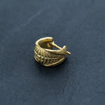 A gold septum ring with intricate, feather-like engravings on a dark, textured surface. The Kaya Movement's Futuristic Xenomorph 18k Gold-Plated Septum Ring for Men and Women is crescent-shaped with a clasp mechanism visible on one end, highlighting the fine details of its biomechanical alien design.