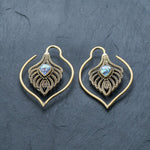 Experience the elegance of Kaya Movement’s Unisex Handmade Brass Leaf Ear Weights with Abalone Shell - Boho Hippie Tribal Earrings. These gold-toned earrings feature a stunning teardrop-shaped abalone shell set in the center, surrounded by intricate metalwork against a dark slate backdrop, ideal for those who appreciate edgy urban fashion and gauged ears jewelry.