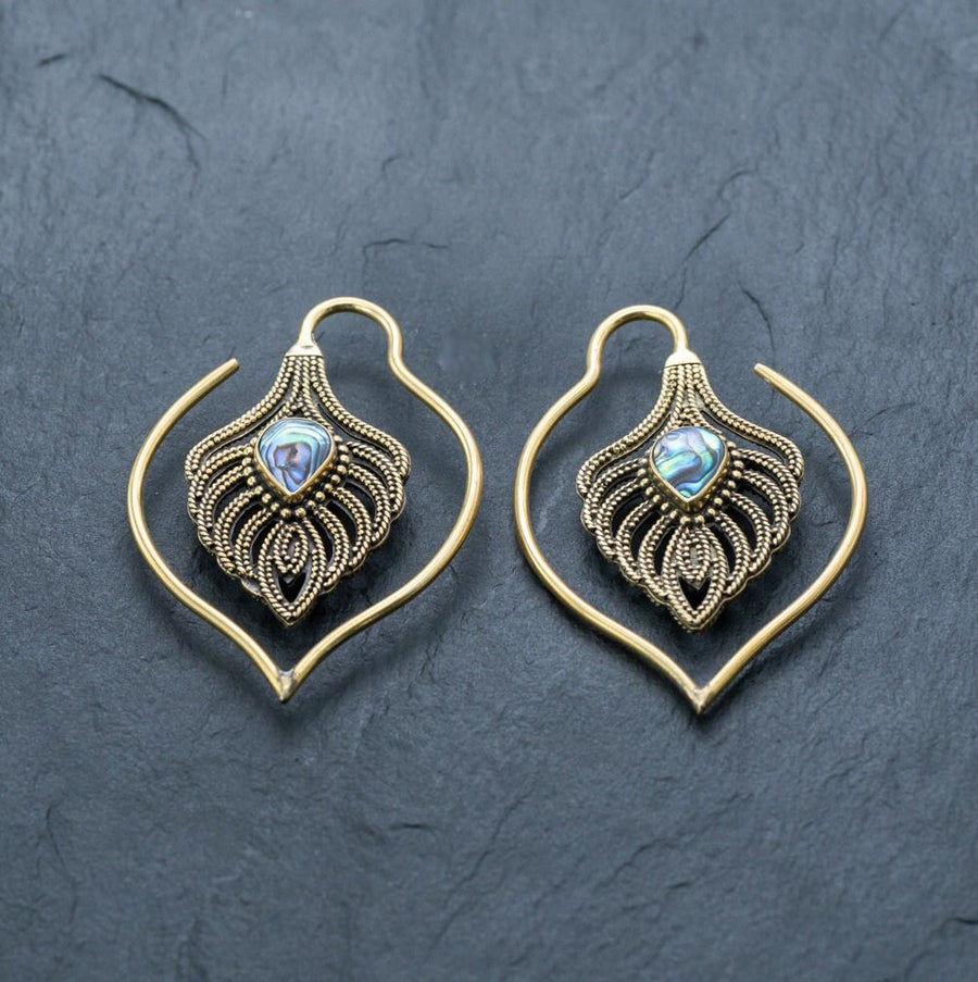 Experience the elegance of Kaya Movement’s Unisex Handmade Brass Leaf Ear Weights with Abalone Shell - Boho Hippie Tribal Earrings. These gold-toned earrings feature a stunning teardrop-shaped abalone shell set in the center, surrounded by intricate metalwork against a dark slate backdrop, ideal for those who appreciate edgy urban fashion and gauged ears jewelry.