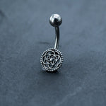 The Kaya Movement Silver Mandala Belly Button Ring boasts an intricate mandala-like design set against a dark, textured background. This boho belly ring features a smooth, curved 9mm surgical steel barbell with a spherical end, making it one of the most exquisite options among navel piercings.