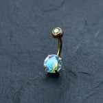 The Kaya Movement 18K Gold Navel Ring, a stunning Crystal Belly Barbell, showcases a large iridescent round opal crystal at the bottom and a smaller matching opal crystal on the top. This hypoallergenic, discreet piercing body jewelry is perfect for those with sensitivities and is beautifully set against a dark, textured background.