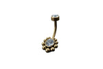 Introducing the Kaya Movement 18K Gold Navel Ring, a stunning piece of body jewelry with a curved barbell design. This hypoallergenic belly barbell highlights a single clear gemstone at the top and features a larger clear gemstone at the bottom, elegantly surrounded by cubic zirconia accents and small gold beads. Perfect for any occasion, it rests beautifully on your skin against a dark, textured background. Rediscover discreet elegance with this allergy-friendly piercing from Kaya Movement.