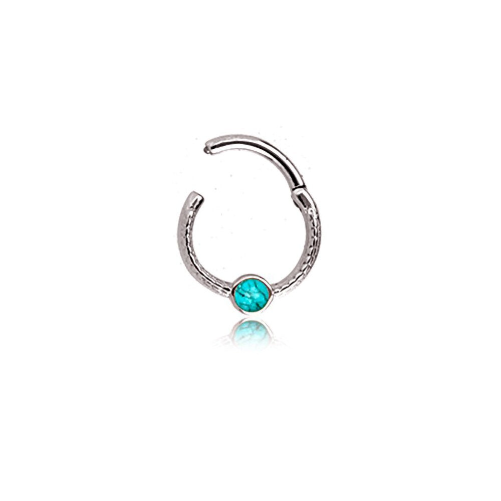 Introducing the "Turia" by Kaya Movement: a minimalist silver-finish septum jewelry piece crafted from 316L stainless steel. This refined and elegant hoop nose ring features a textured design with a small turquoise gemstone at its center, perfect for the nose, tragus, or lobe. It has a sleek design measuring 1.2mm and includes an open, adjustable end for easy insertion and removal. The vibrant blue accent of the gemstone stands out beautifully against its polished silver finish.