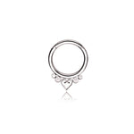 The Zuri Minimalist Mandala-Inspired Septum by Kaya Movement, crafted from silver 316L steel with a 1.2mm gauge and 8mm diameter, features a round design showcasing a symmetrical arrangement of small spheres and a stylized heart at the bottom center. This simple yet elegant piece exudes charm, set against a plain white background.