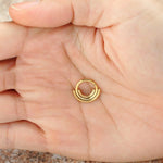 A close-up image of a hand holding the Lira Minimalist Boho Chic Septum in 316L Steel Gold PVD Finish from Kaya Movement. The palm is open, showcasing the refined gold Bohemian jewelry piece with its modern style. The background is blurred and indistinct, highlighting the septum's elegant design and craftsmanship.