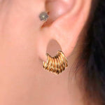 Close-up of an ear adorned with a Kaya Movement Aurel Simple Ear Ring in 316L Steel Gold PVD Finish, featuring multiple gold rings clustered together. The hoop earring, available in gauges of 2 or 3mm and diameters of 8, 10, 12, and 14mm, is complemented by a small decorative flower-shaped stud on the upper part of the ear for a touch of minimalist elegance. The background is blurred to emphasize the earrings.