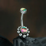 The "Bohal Navel Jewelry - Boho Essence with Abalone Shell" by Kaya Movement is a curved 316L surgical steel belly button ring featuring two vibrant abalone shell inlays. The larger inlay, surrounded by delicate metal beads, adorns the bottom while the smaller one sits gracefully at the top, truly embodying natural and bohemian elegance against a blurred and dark background.