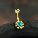 The Kaya Movement's Bohal Navel Jewelry - Boho Essence with Abalone Shell is a stunning piece crafted from 316L surgical steel with a gold finish. This elegant navel jewelry features two turquoise stone accents: a small, simple round setting on top and a larger circular turquoise piece surrounded by gold beads at the bottom, all masterfully displayed on a dark surface. Embrace natural and bohemian elegance with this exquisite jewelry item.