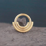 Close-up of the Kaya Movement Lira Minimalist Boho Chic Septum in refined gold PVD finish, featuring a unique design with three semi-circular, parallel bands extending from the main circle. The 316L steel septum ring, with a 1.2mm gauge and an 8mm diameter, is placed on a rough, textured rock surface against a dark blue and gray gradient background.