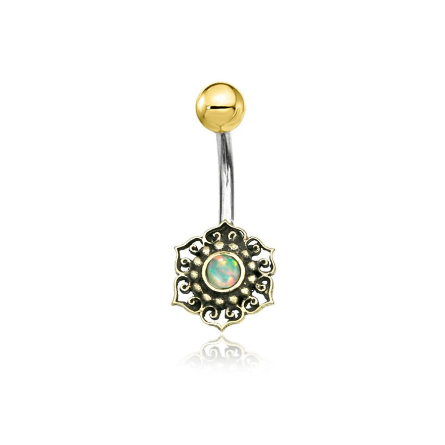 The Lutia Navel Jewelry by Kaya Movement is a boho-hippie festival accessory that features an exquisite mandala lotus design with a turquoise gem. This handcrafted belly button ring combines brass and surgical steel, showcasing a gold ball on one end and an intricate gold setting with a central turquoise stone on the other, all elegantly crafted on a curved silver bar.