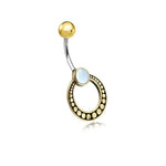 The Azmi Navel Jewelry by Kaya Movement features a Boho Ethnic design with a curved surgical steel barbell. Topped with a gold ball and centered with an exquisite mother of pearl stone, this unique handmade festival accessory is adorned with a circular brass pendant, accented by raised gold dots around its perimeter.