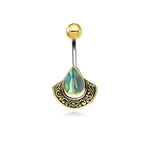 Introducing the Lumi Navel Jewelry by Kaya Movement: a stunning piece of handcrafted jewelry that effortlessly combines elegance and boho style. This unique festival gem features a surgical steel barbell with a rounded ball at the top, while the bottom charm showcases an iridescent, teardrop-shaped abalone shell set in an ornate brass frame adorned with intricate, swirling designs.