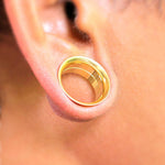 A close-up of an ear with a stretched earlobe showcasing the Zuri Tunnel by Kaya Movement, a gold PVD-finished ear plug in 316L surgical steel. The minimalist design highlights the elegance of the jewelry, contrasted beautifully against the smooth and well-maintained skin around the earlobe. Available in 6mm and 16mm sizes.