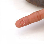 A hand with a finger outstretched holds a small, rose gold Liora Elegant Septum ring by Kaya Movement delicately balanced on the fingertip. The background is white, and the stainless steel 316L ring is detailed with a pattern of small, round beads along part of its circumference.