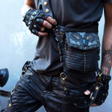 Close-up of a person wearing a black leather outfit with intricate designs and gold detailing, perfect for dystopian festivals. The outfit includes fingerless gloves and the SHIPIBO Tribal Apocalyptic Leather Belt & Shoulder Bag | Labradorite by Kaya Movement, adorned with metal accents. They also have tattoos on their arm, set against a plain light gray wall.