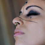 Side profile of a model wearing the DARMA brass septum clicker and ornate earrings.